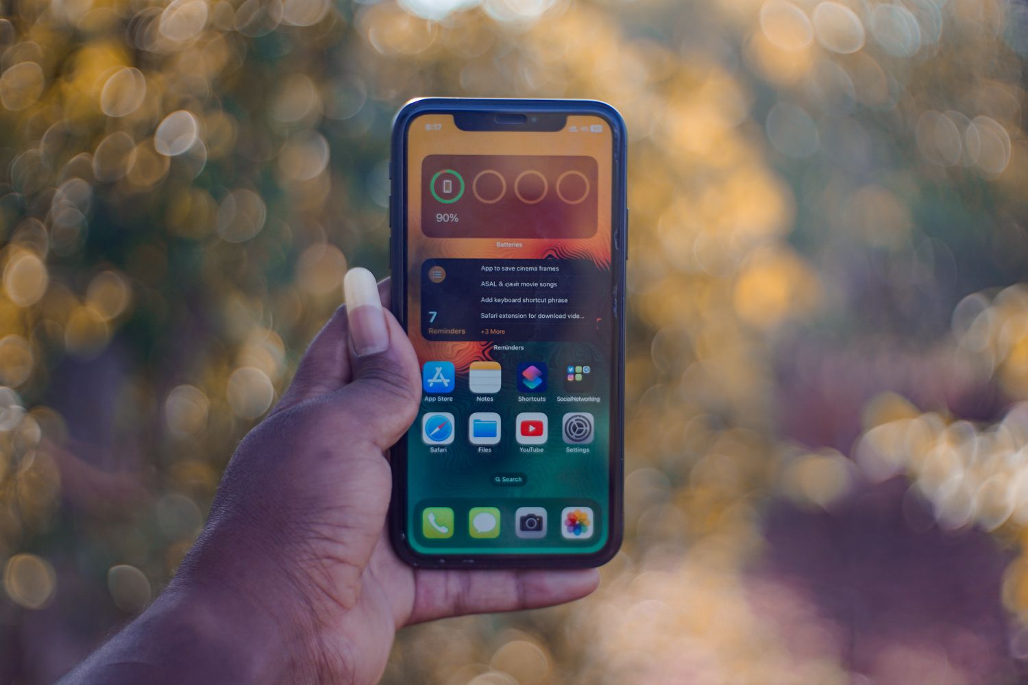 Main tenant un smartphone affichant des applications, en extérieur